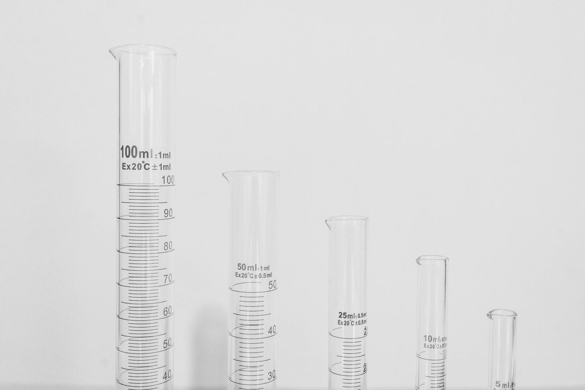 Close-up of various laboratory glassware including test tubes and measuring cylinders on a white background.